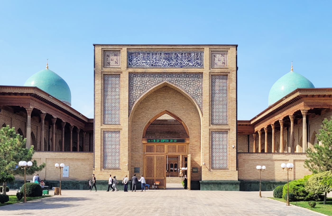 The Hazrati Imam Mosque: a tall tiled portal between two turquoise domes and wooden galleries