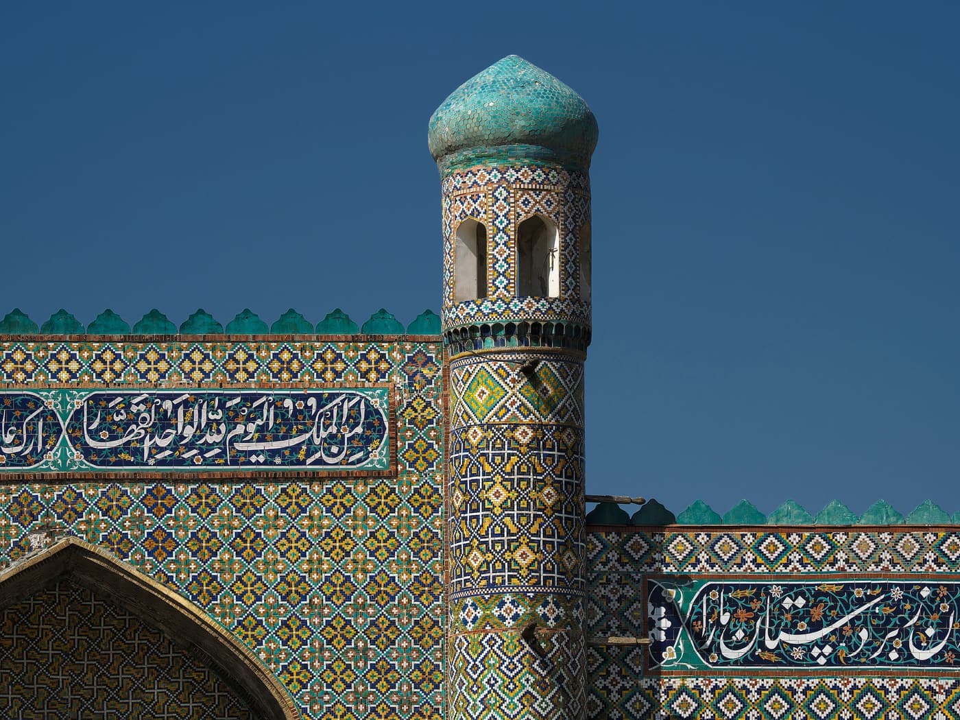 A tiled tower and a band of Arabic script on the palace façade