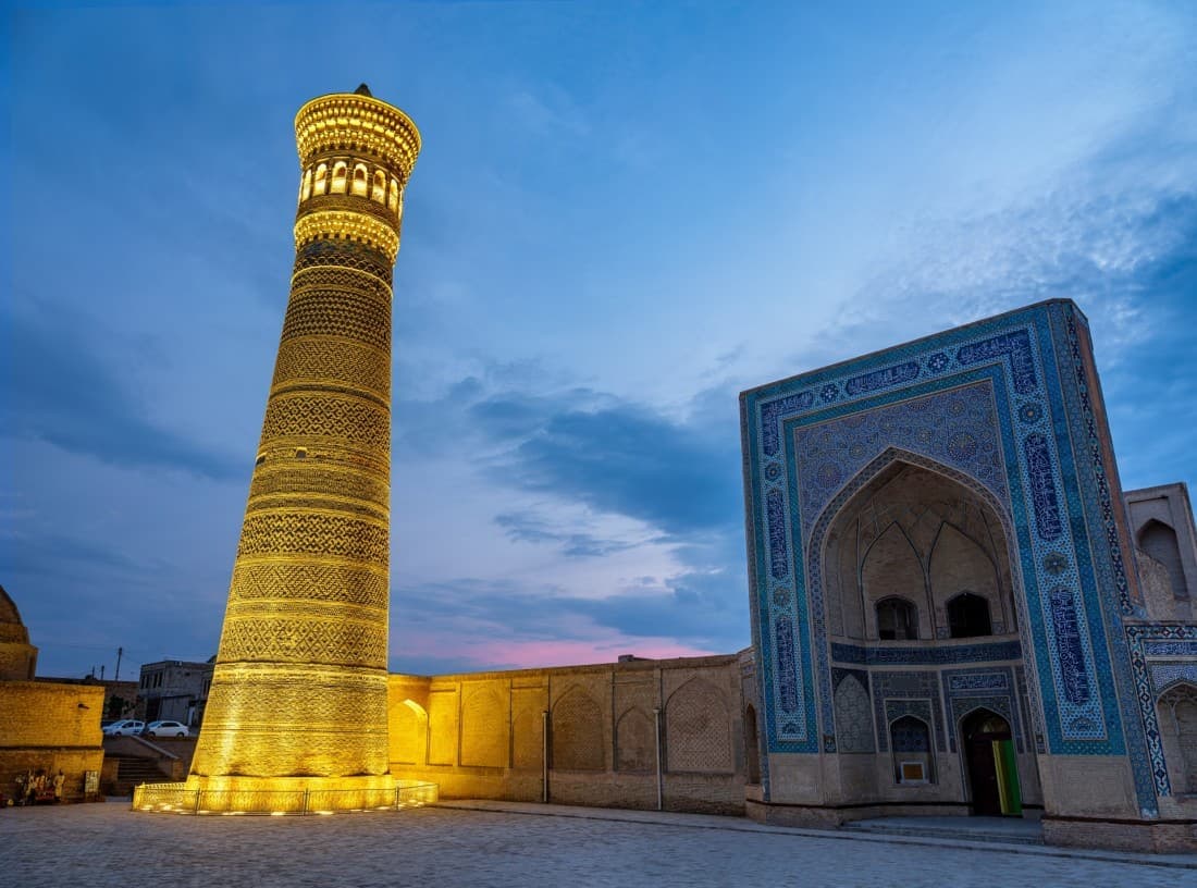The Kalyan Minaret lit gold at dusk beside the portal of Mir-i-Arab